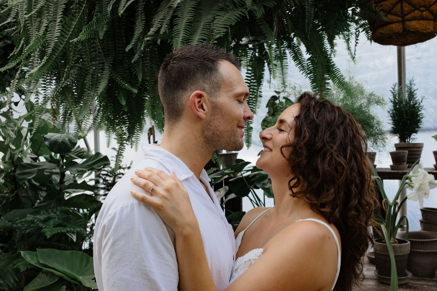 A romantic moment captured in a greenhouse setting with hanging ferns.