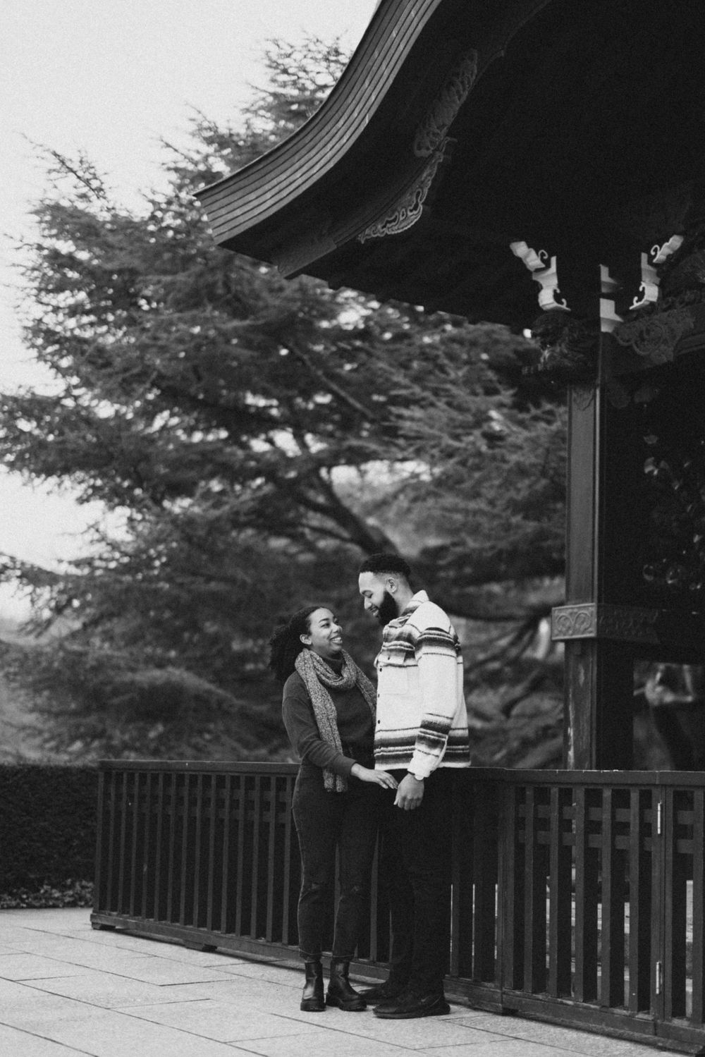 A romantic black and white photo of a couple beneath the eaves of a traditional Japanese pavilion.