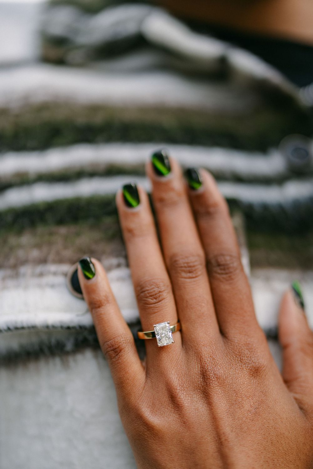 A close-up of a hand wearing green nail polish and displaying an engagement ring.
