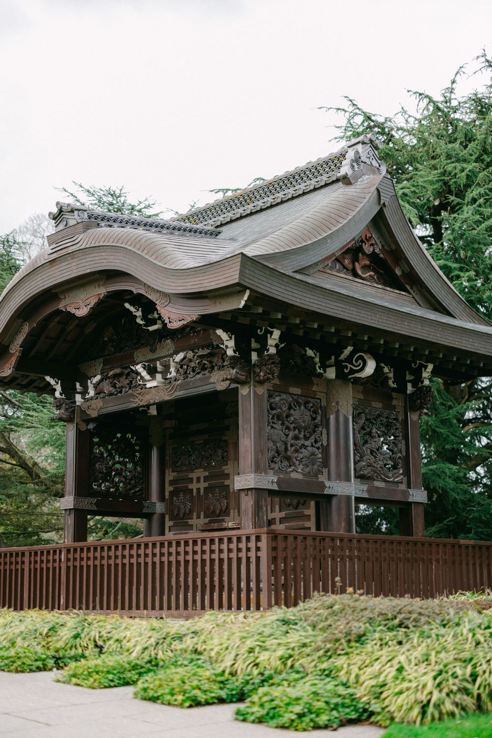 Traditional Japanese wooden pavilion with curved roof and ornate details in a garden setting.