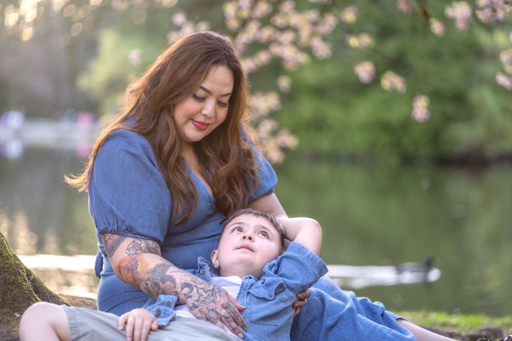 Mother and child share peaceful moment by lake with cherry blossoms in background.