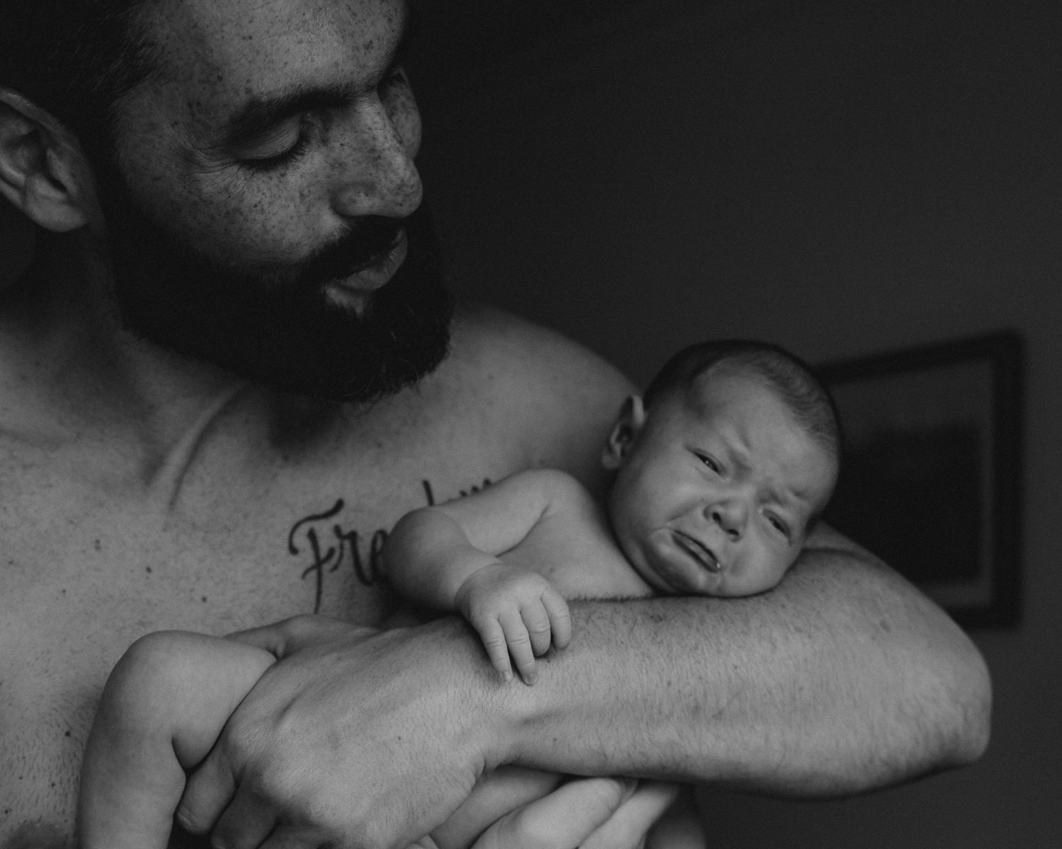 foto em preto de branco de pai e filha recém nascida, pai sorri bebé faz cara de choro em fotografia família Caldas Da Rainha