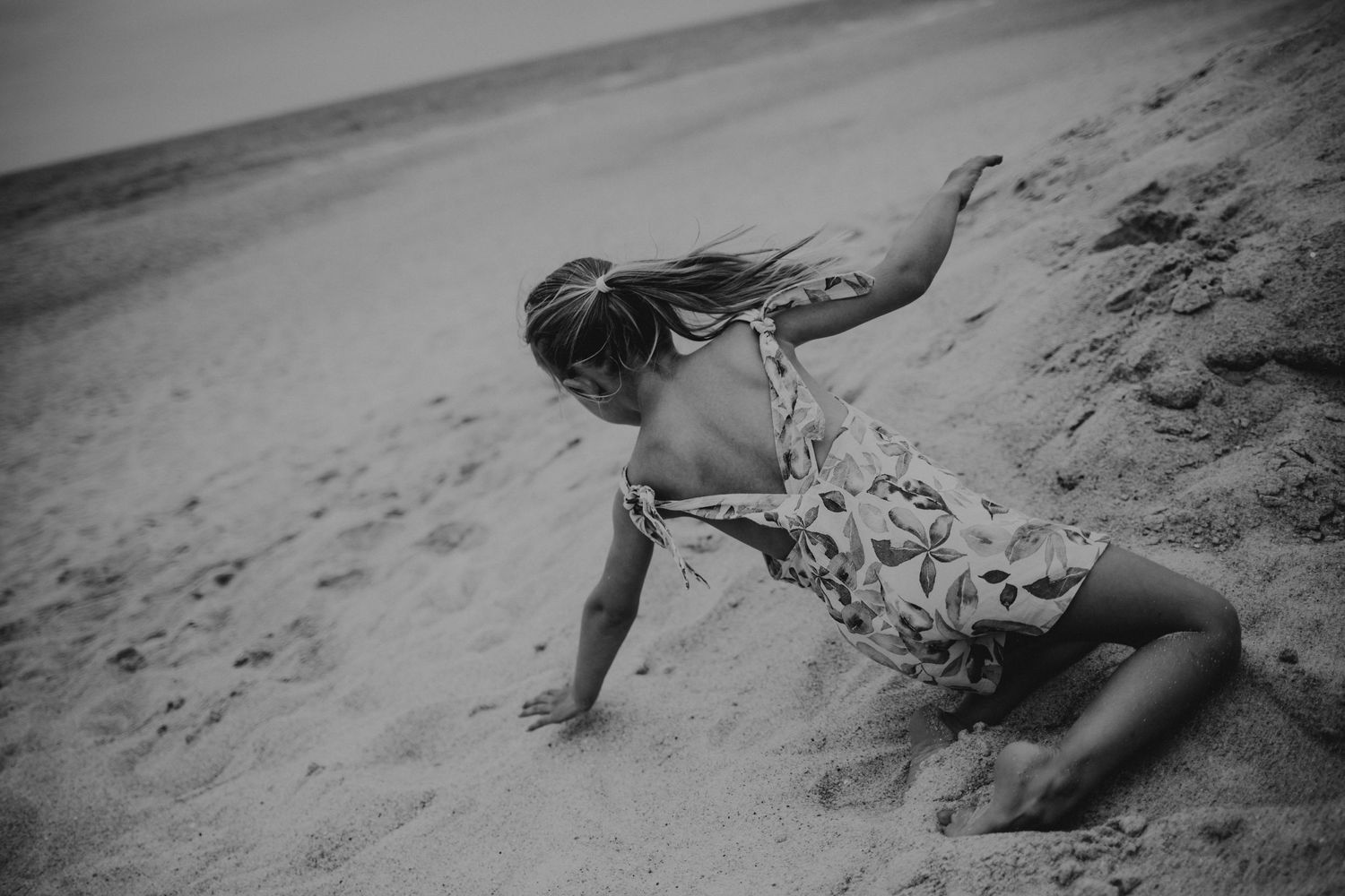 Foto preto e branco de menina a brincar na areia da praia Do Salgado durante sessão fotográfica de família