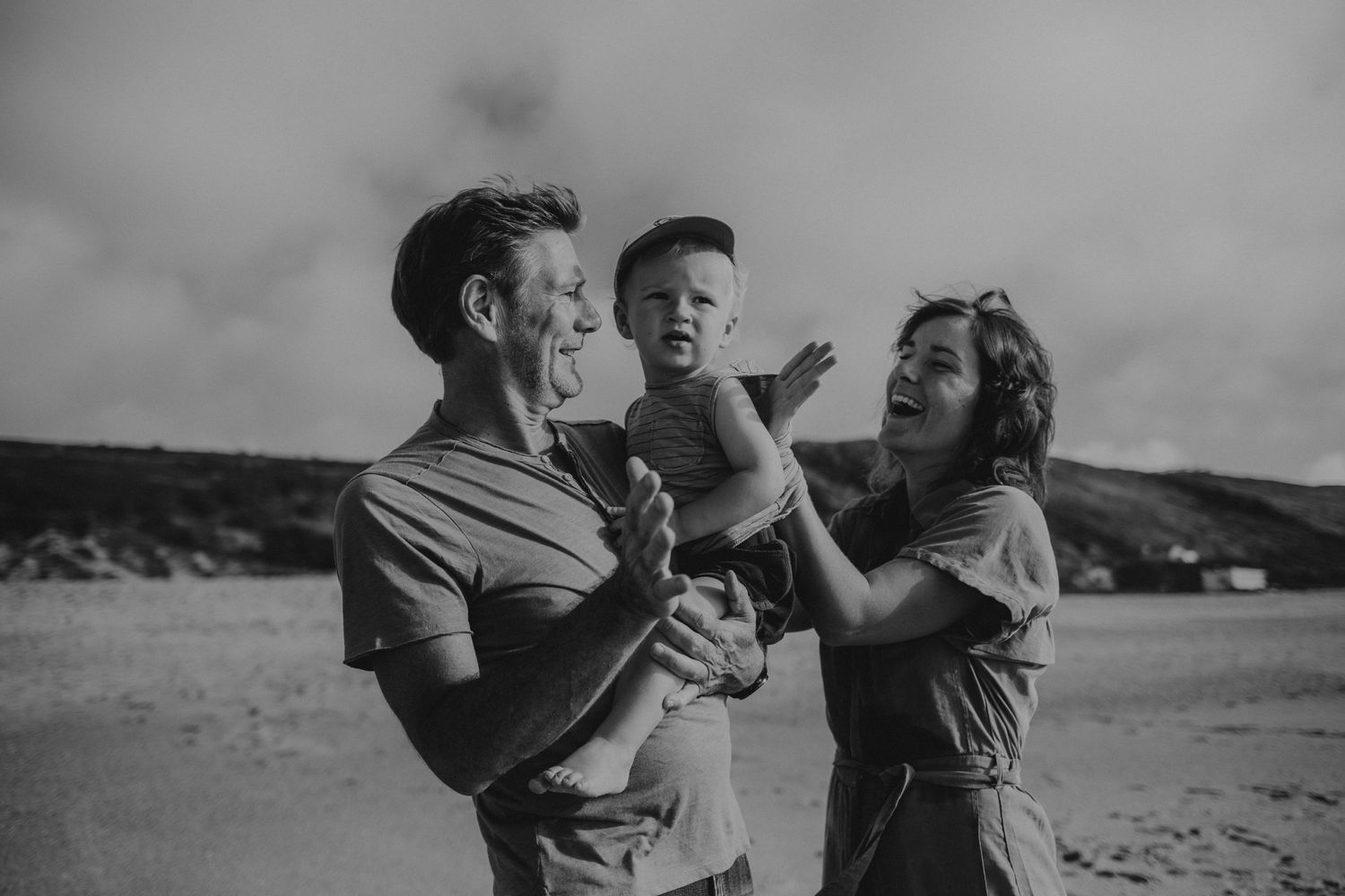 foto preto e branco pai, mãe e filho no colo com detalhe asas anjo na praia do Salgado durante sessão fotográfica de família