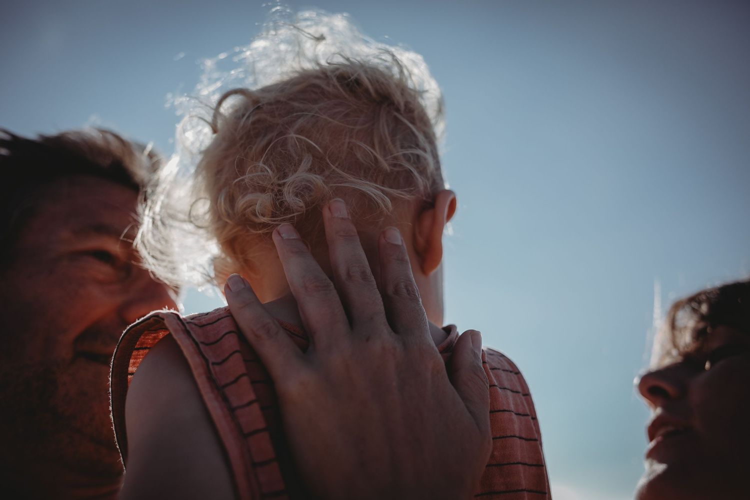 foto colorida pai, mãe e filho no colo detalhe mão com  na praia do Salgado durante sessão fotográfica de família