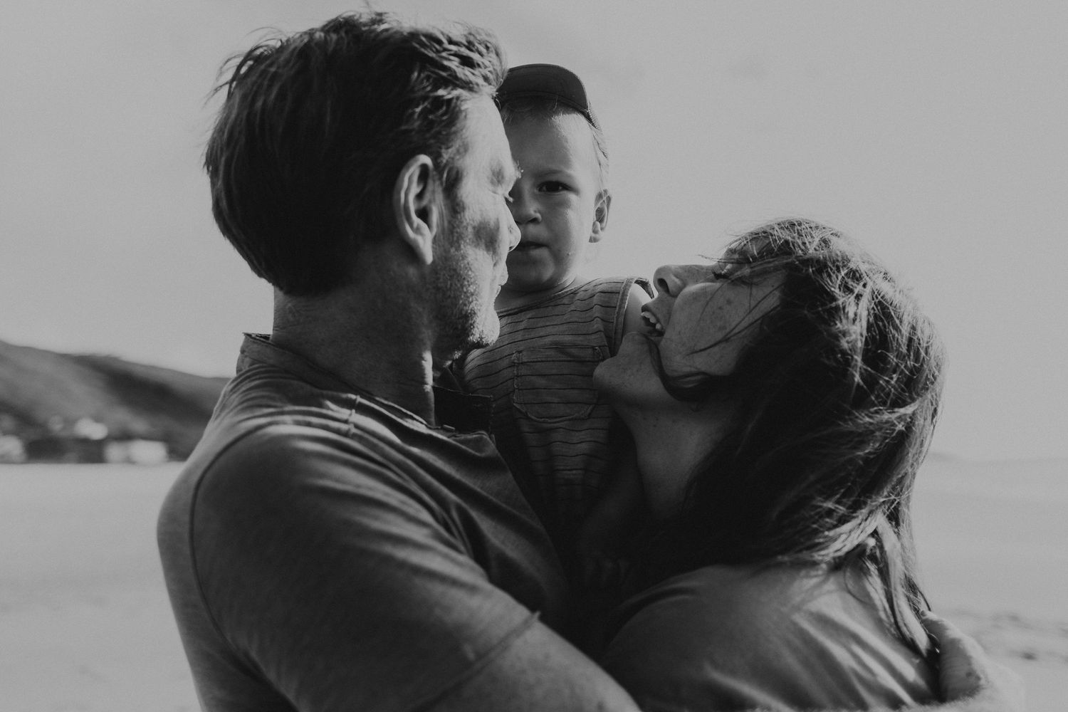 foto preto e branco pai, mãe e filho no colo com  na praia do Salgado durante sessão fotográfica de família