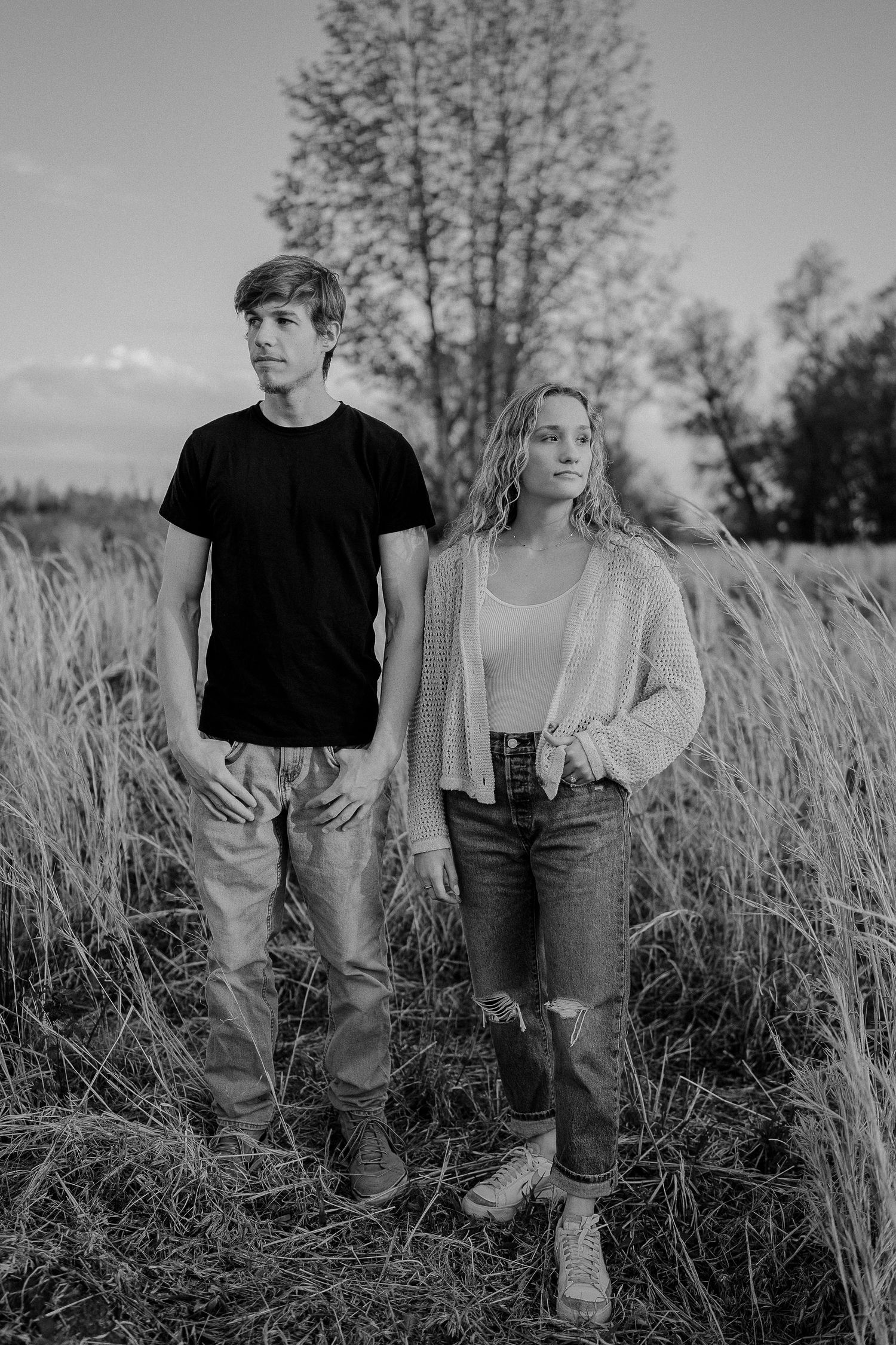 Two people stand together in a field of tall grass during golden hour.
