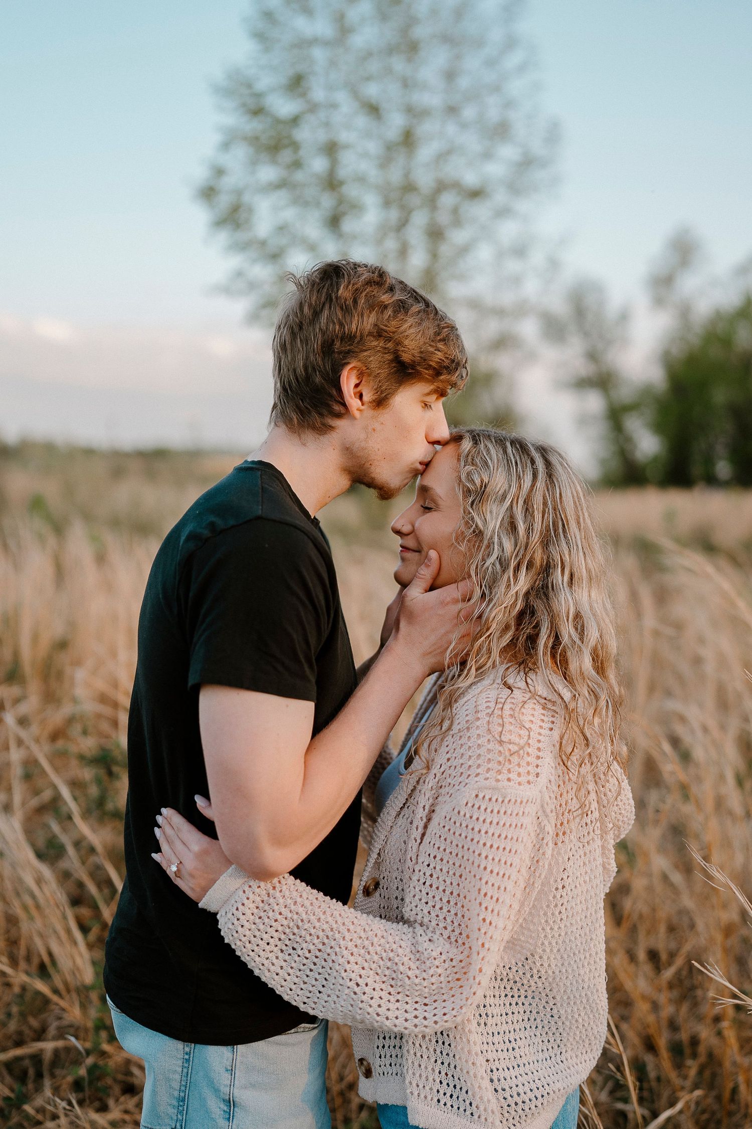 A tender moment between two people in a sunlit field of tall grass.