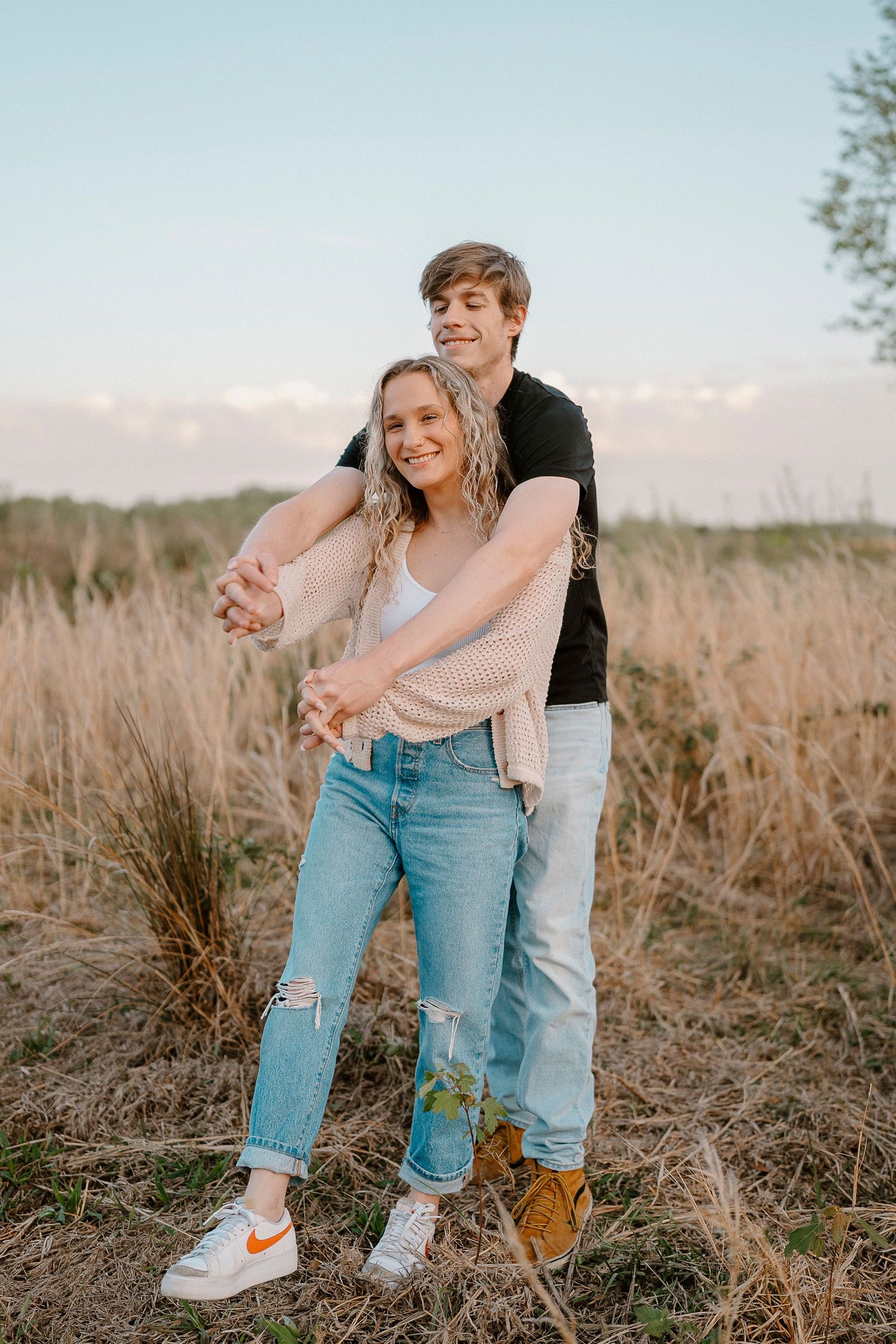 A playful embrace between two people in casual wear standing in a golden field.
