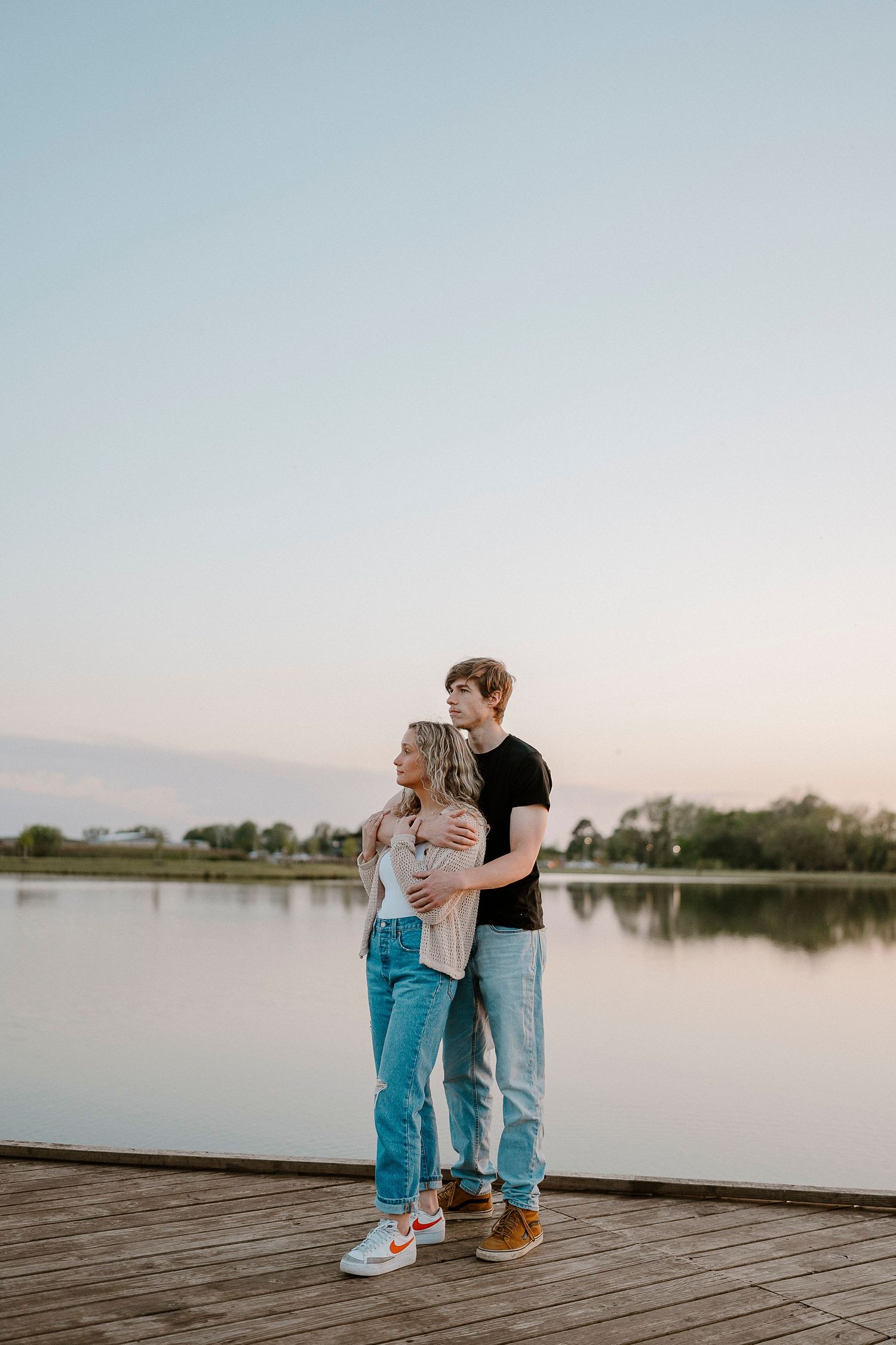 Couple sits together on wooden dock overlooking serene lake at sunset.