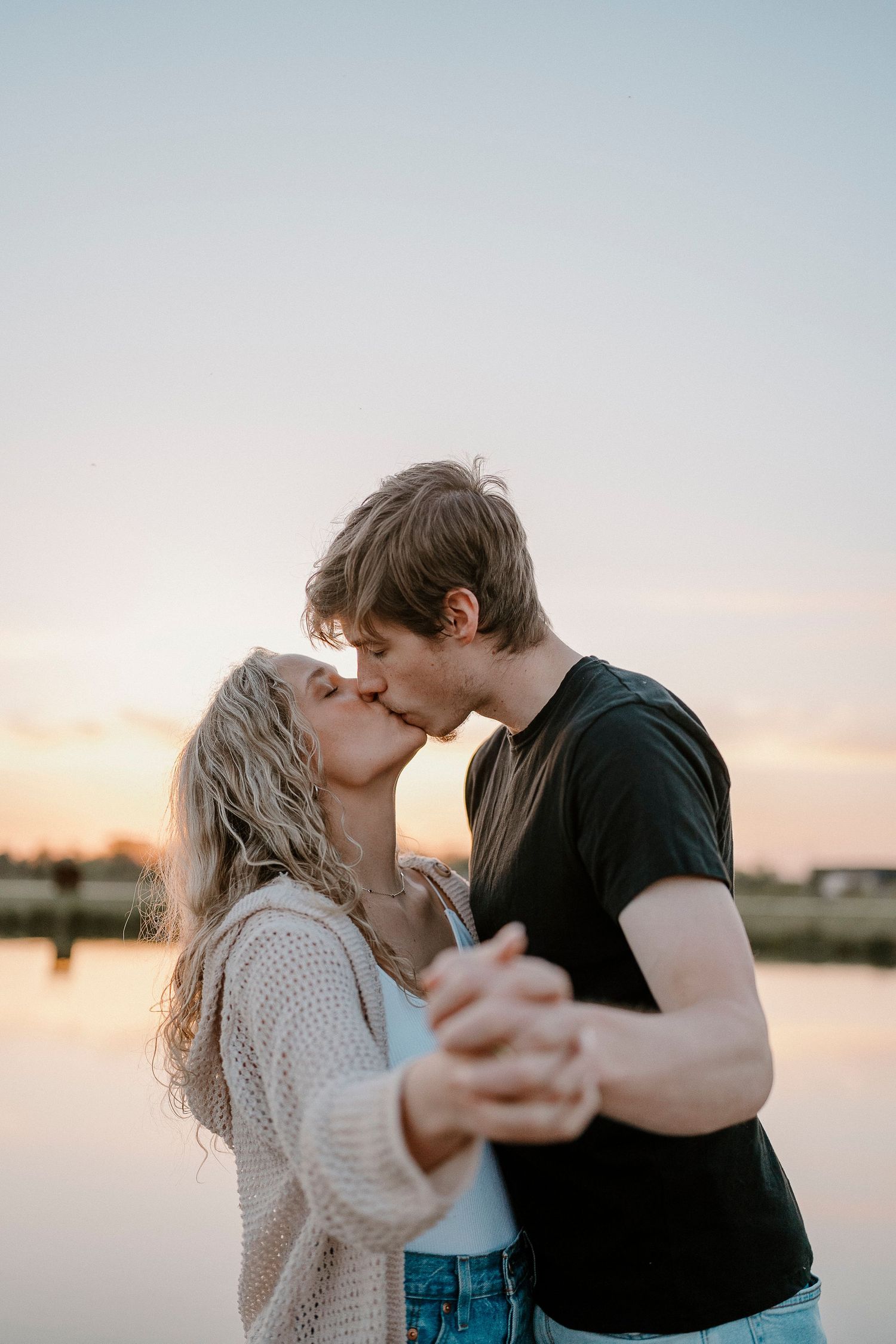 Romantic couple embraces while sharing tender moment by the water during sunset.