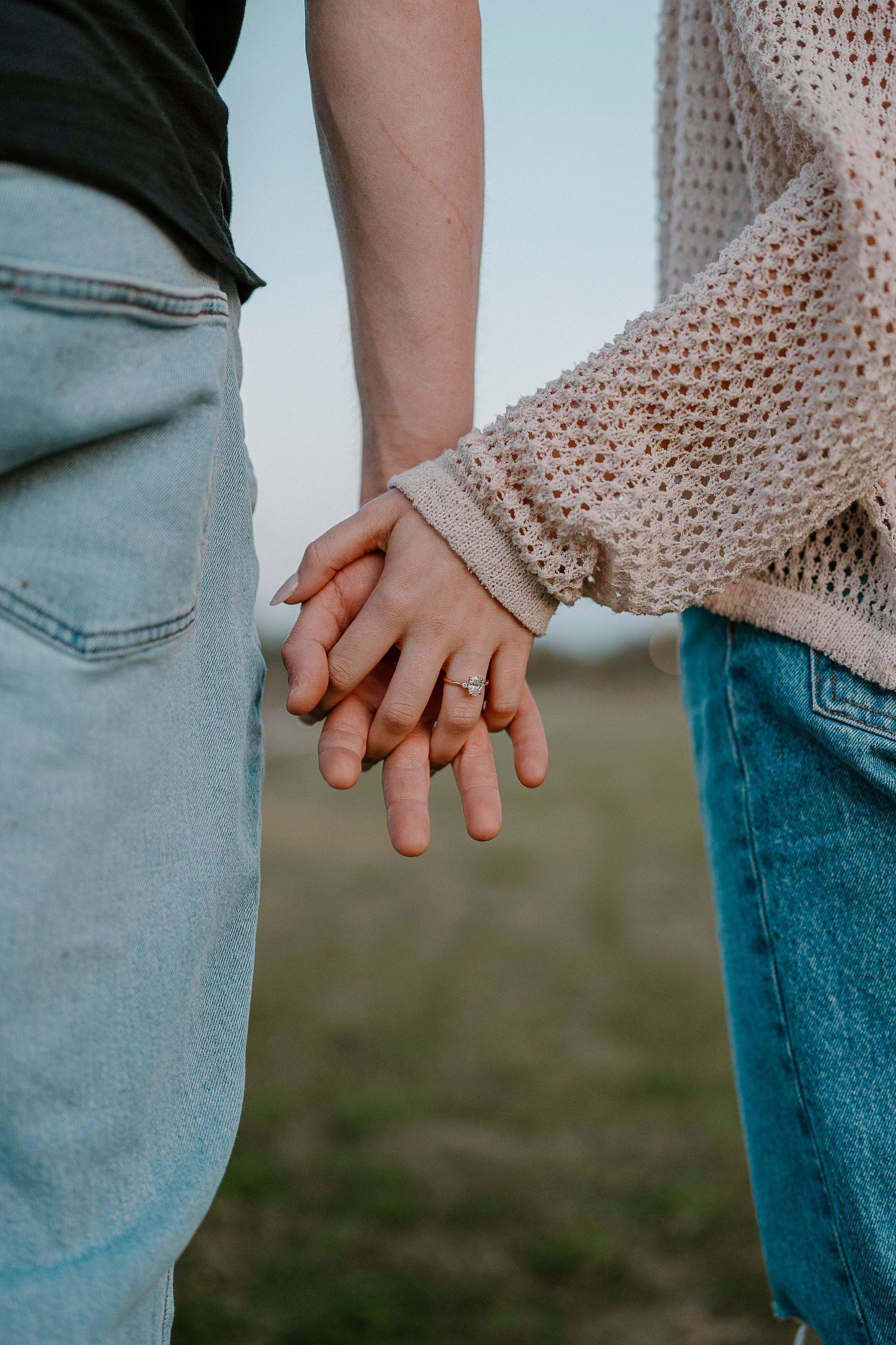 Close-up of two people holding hands wearing jeans and knit sweater.
