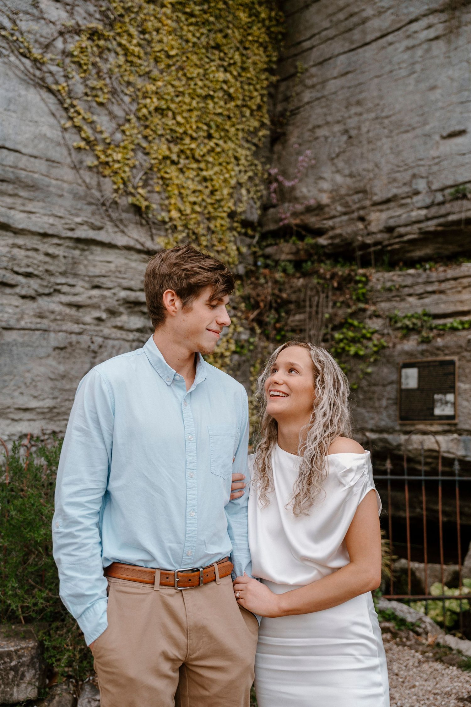 Couple in coordinated outfits share loving glances against stone wall backdrop.