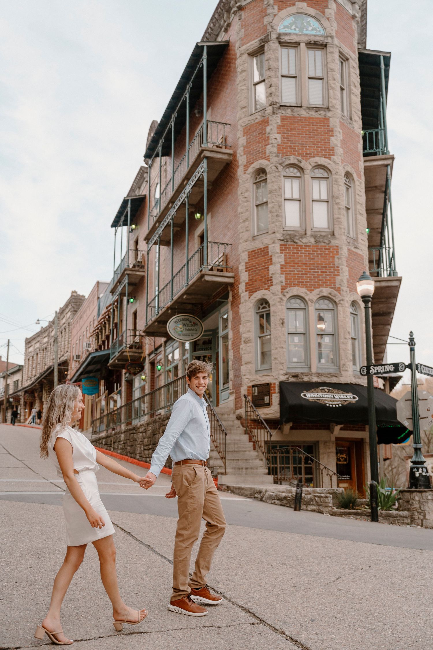 Playful couple walking along historic brick building sidewalk.