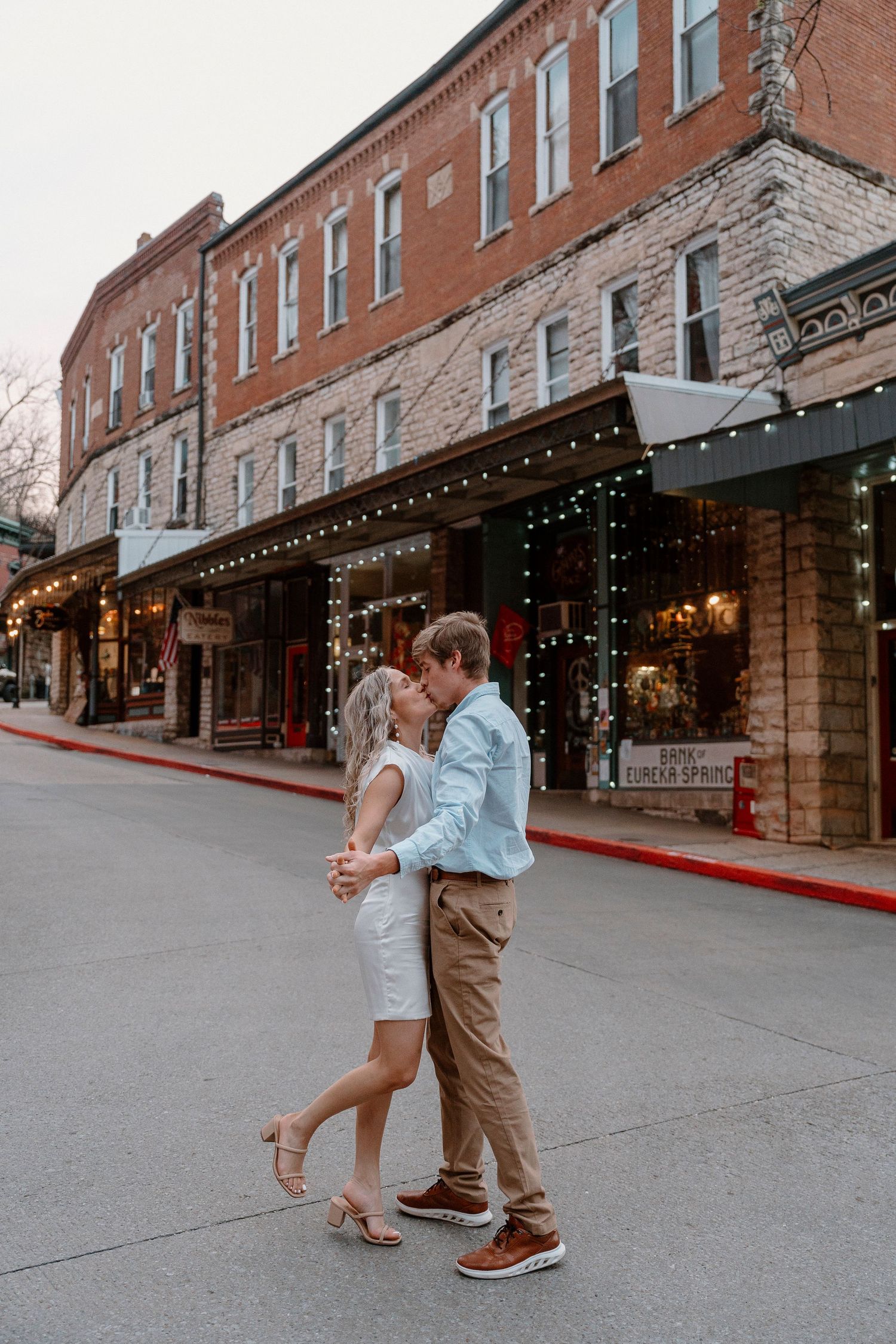 Romantic dance scene on city sidewalk with string lights and brick buildings.