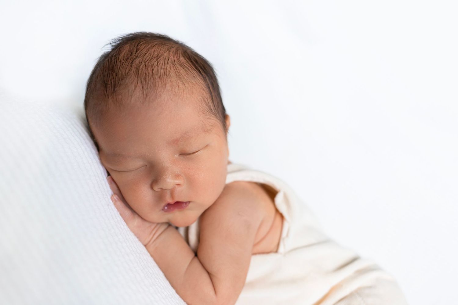 Peaceful sleeping newborn baby swaddled in white wrap against white background.