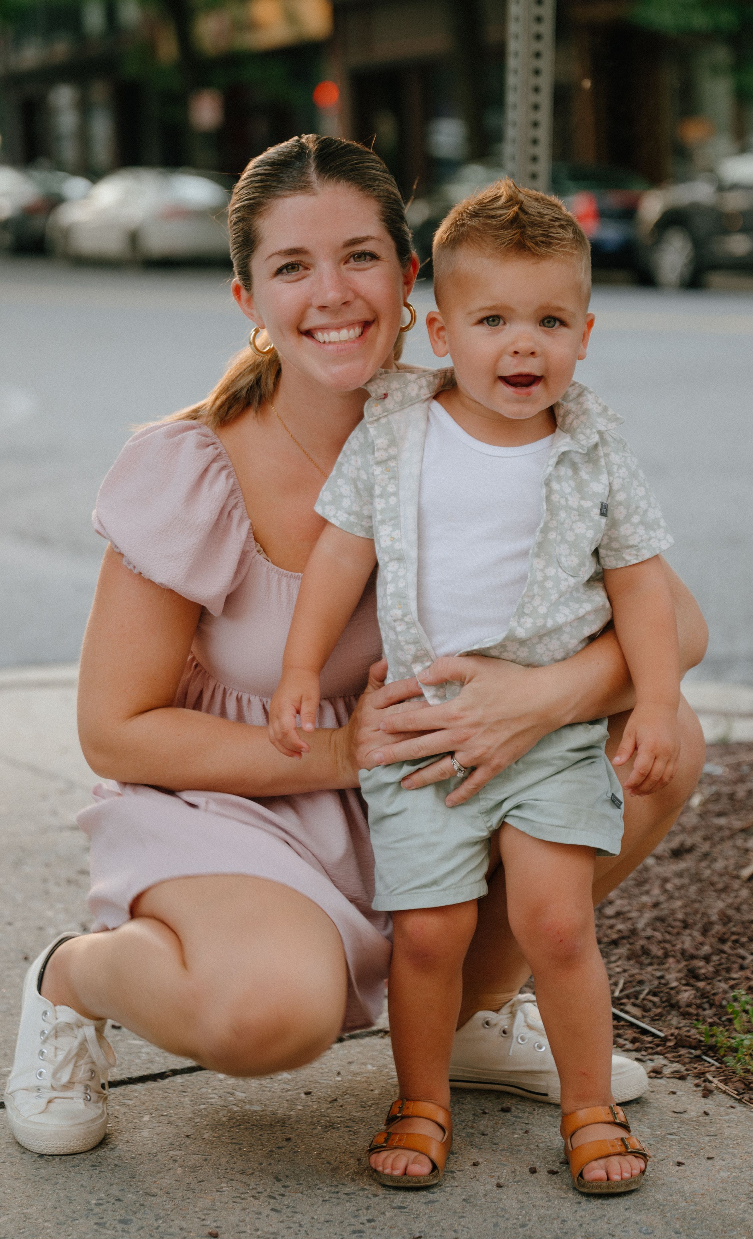 A cheerful parent and child moment outdoors on a sunny city sidewalk.