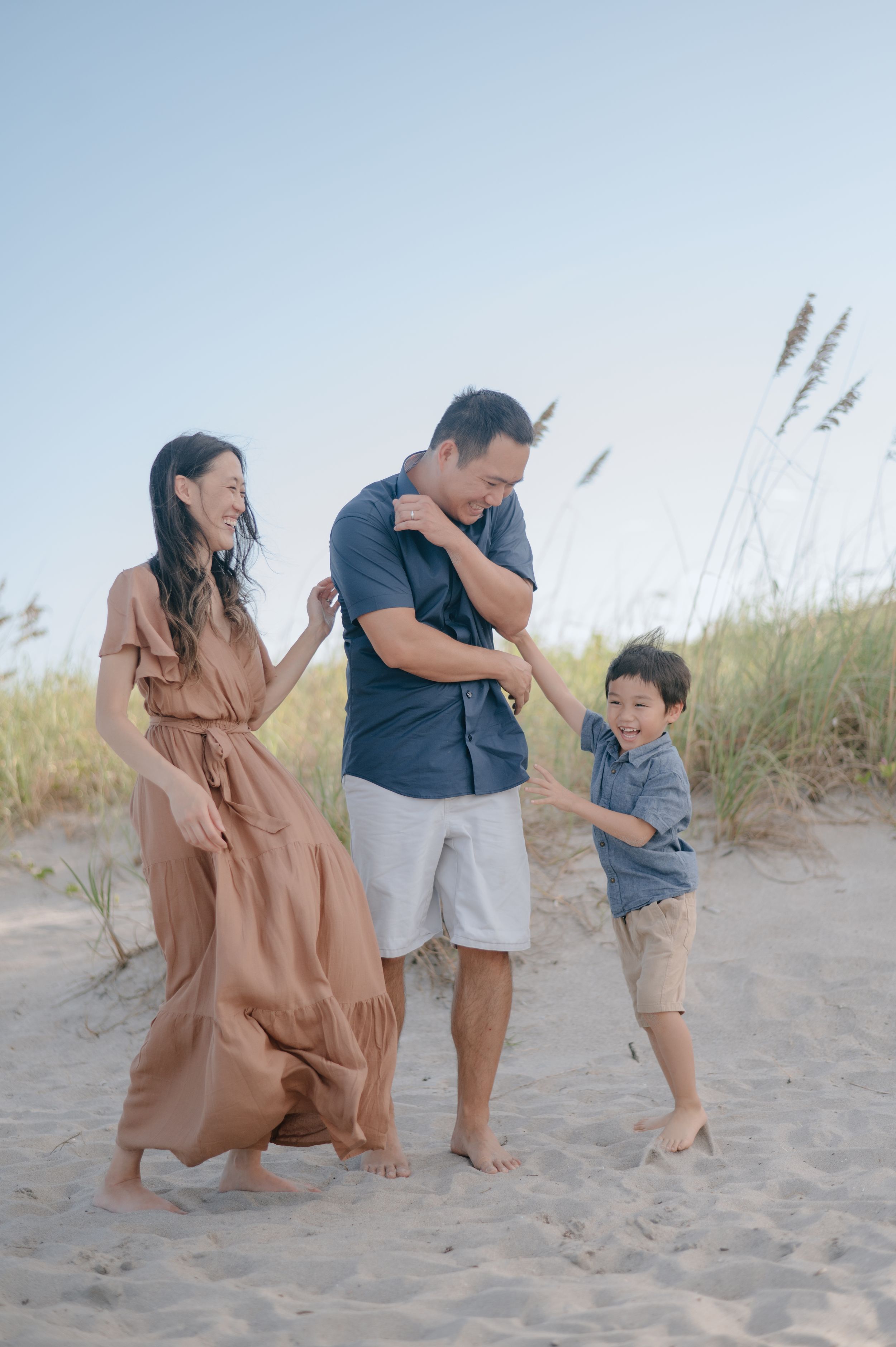 Family of three having fun together on a sandy beach with tall grass in the background.