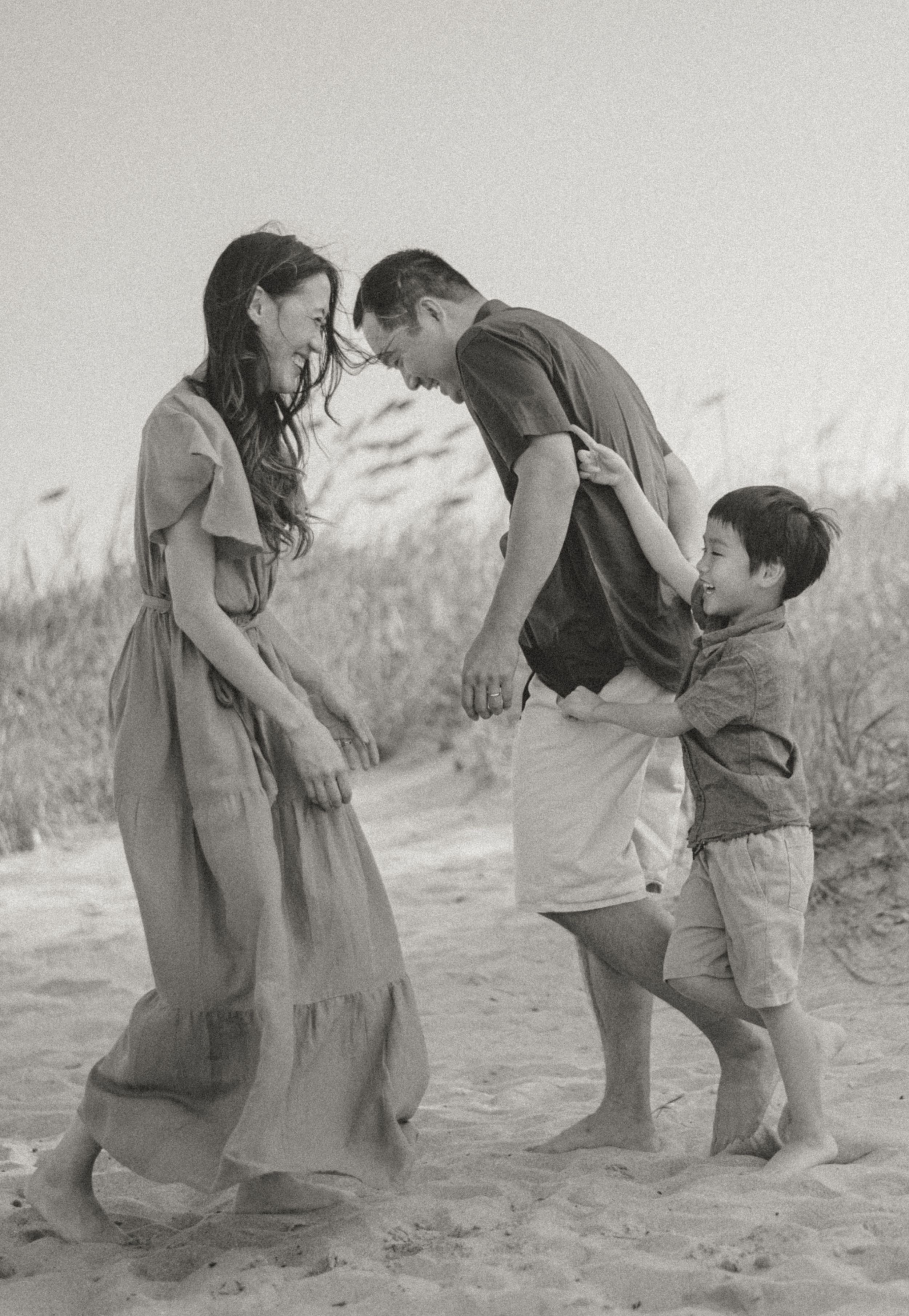 Black and white photo of a family sharing a playful moment on beach sand.