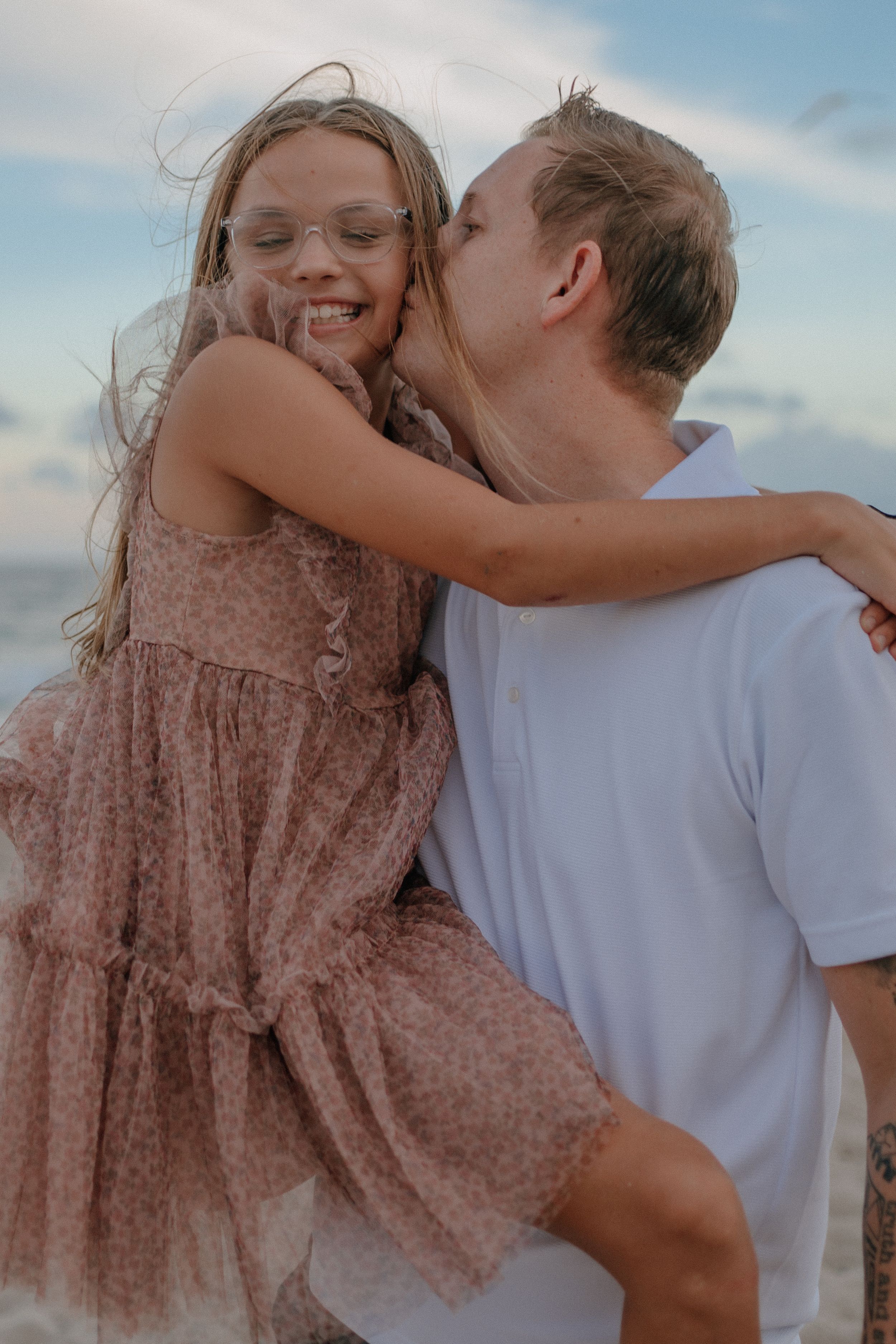 Playful beach portrait showing joyful moment between parent and child in matching casual attire.