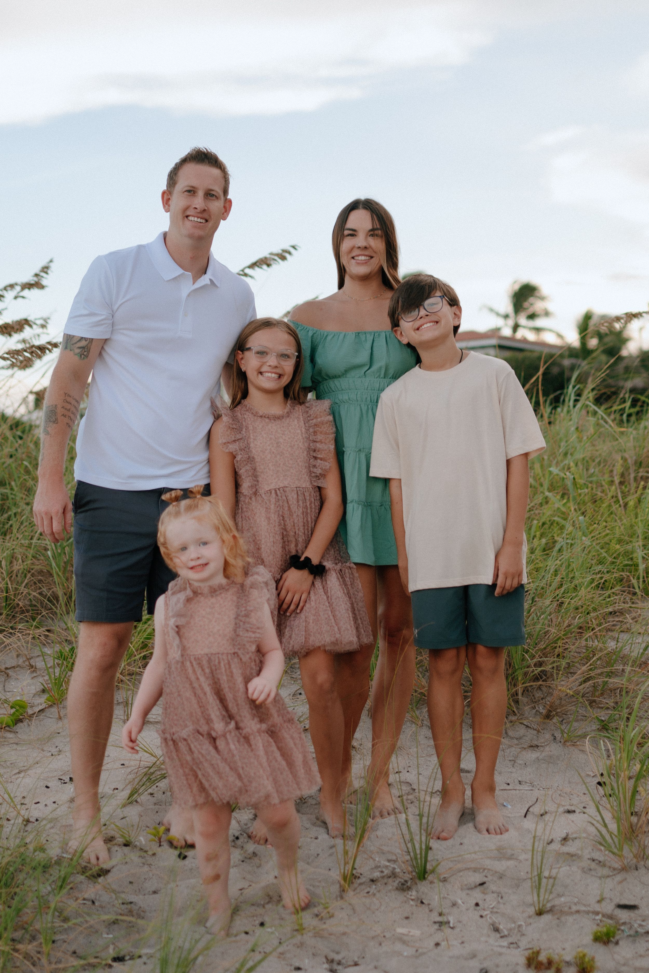 Family portrait on a breezy beach path with coordinated outfits in pink, white and green.