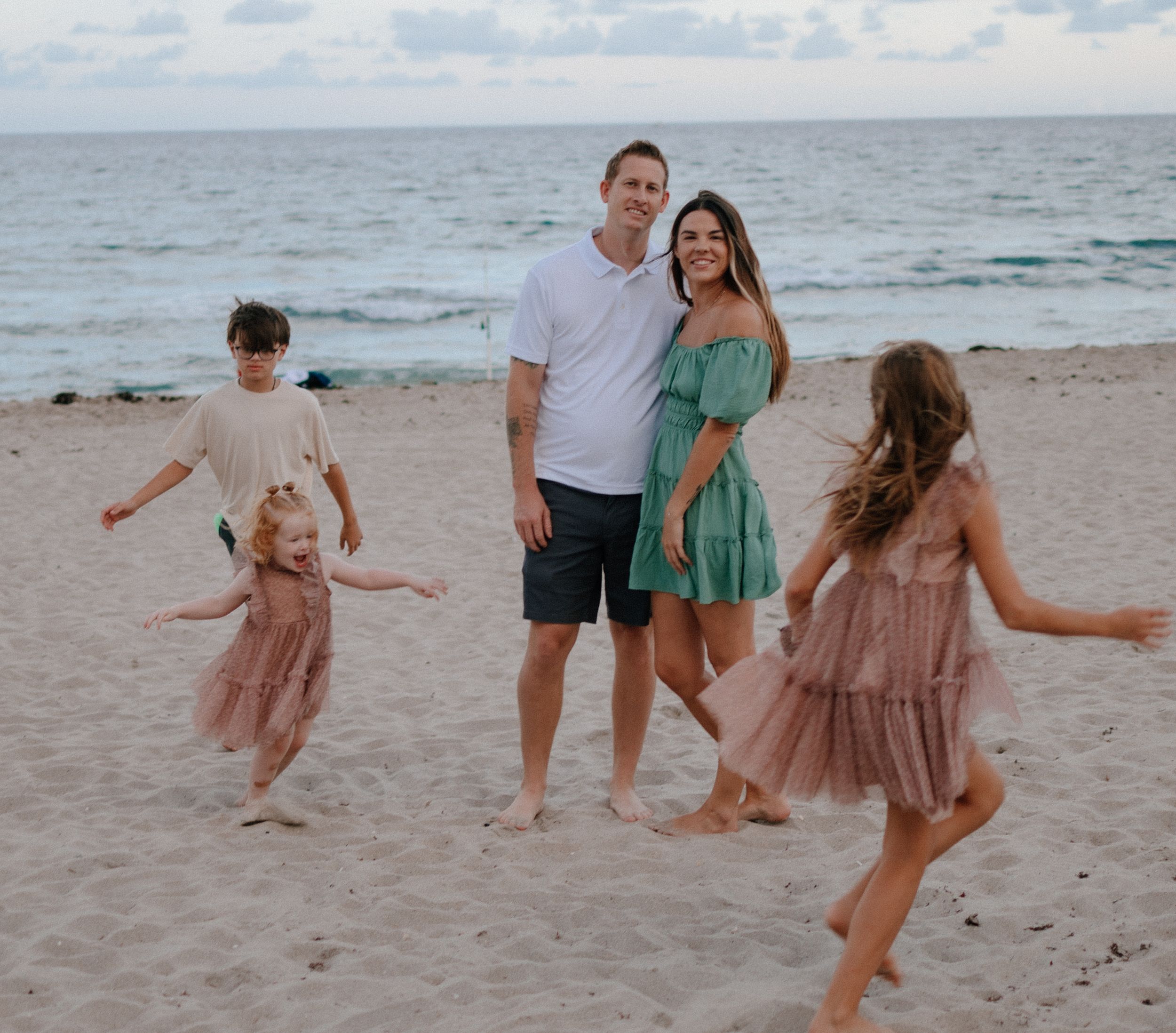 A beach family photoshoot at sunset showing carefree fun and coordinated outfits in pink and green.