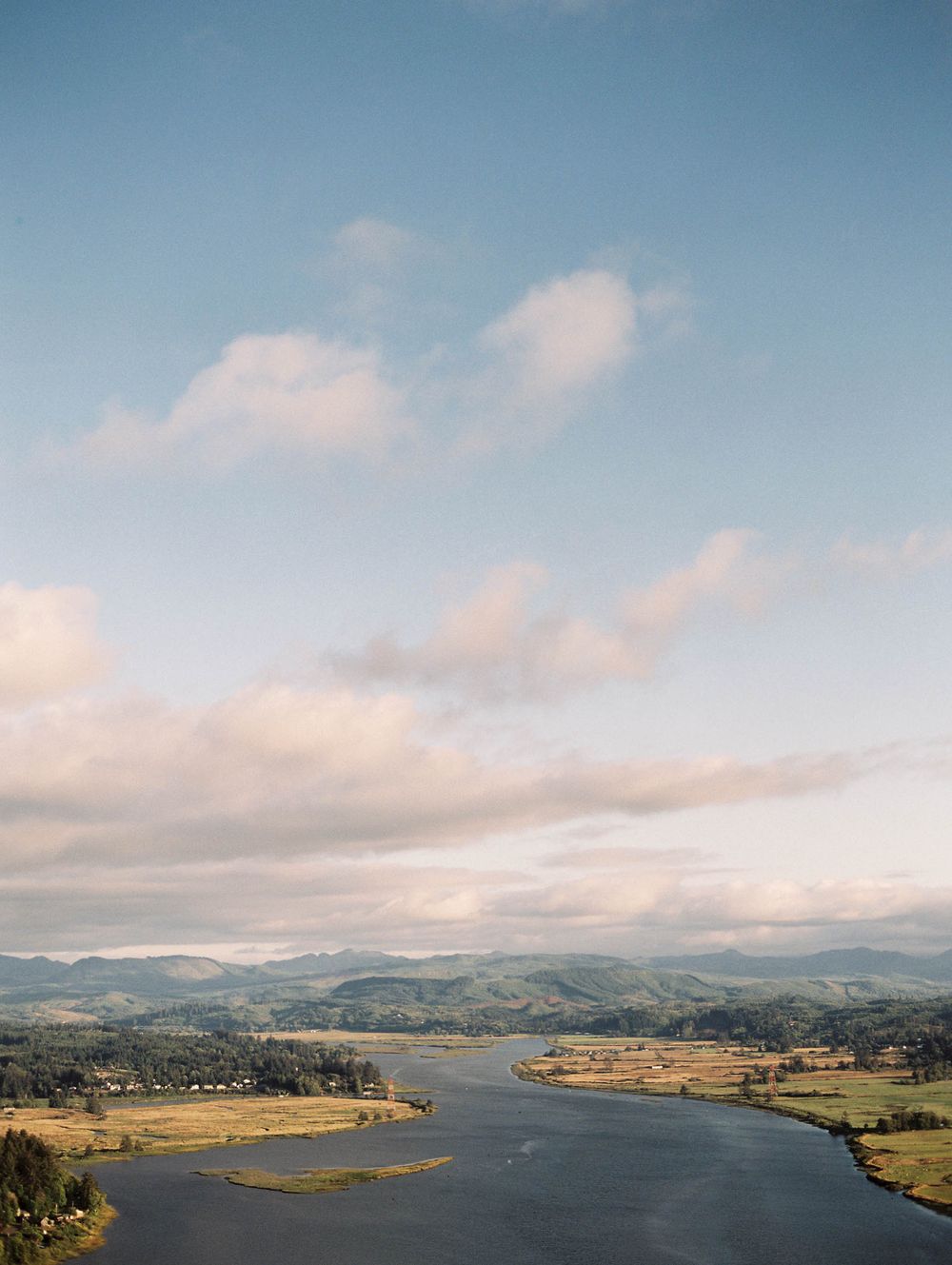 Aerial view of winding river through lush green valley with mountains and clouds in Oregon landscape.