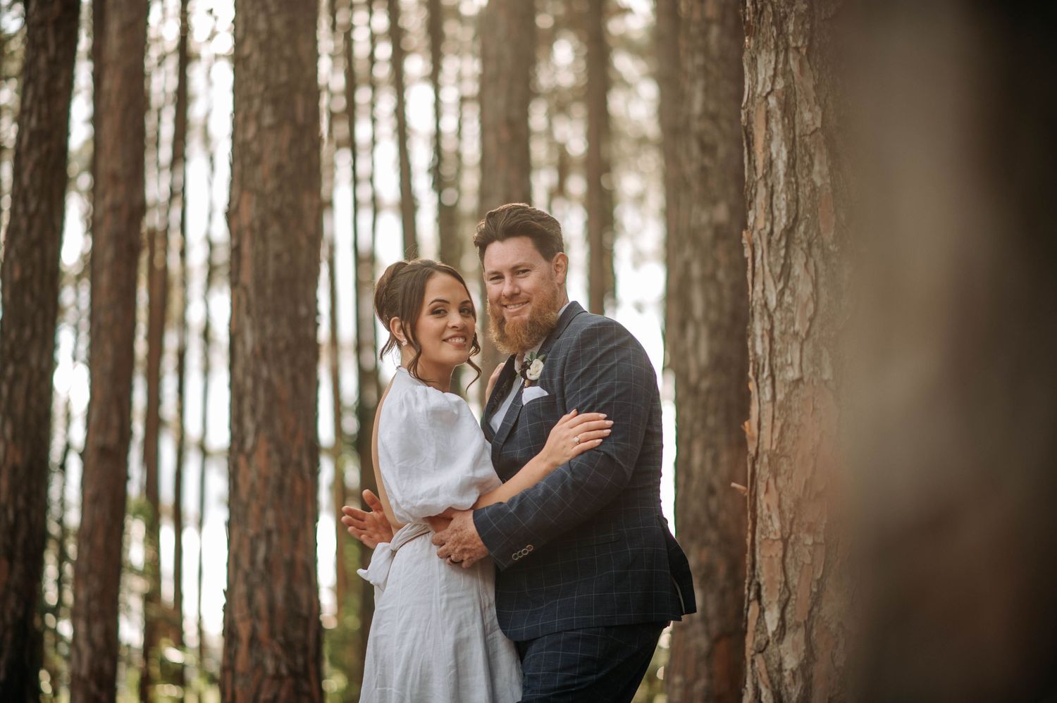 Intimate wedding portrait of couple embracing among tall pine trees.