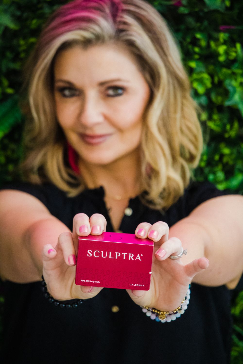 Close-up product shot of pink Sculptra box held against green plant background.
