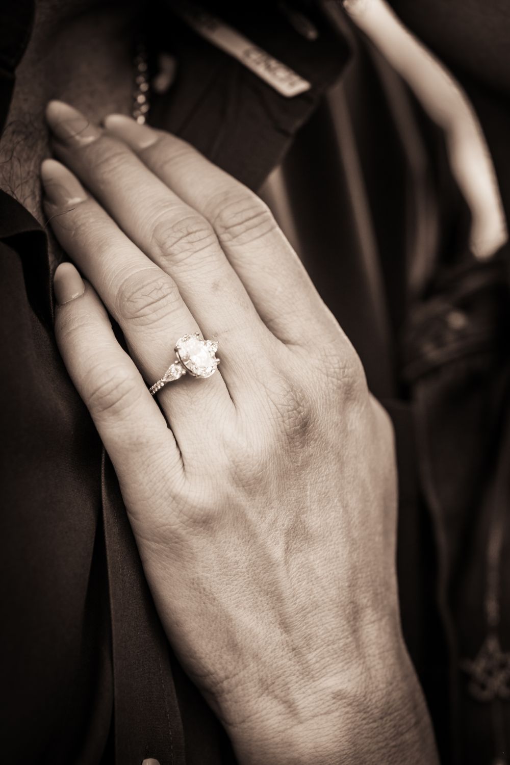 A close-up black and white photo of a hand wearing an elegant engagement ring.