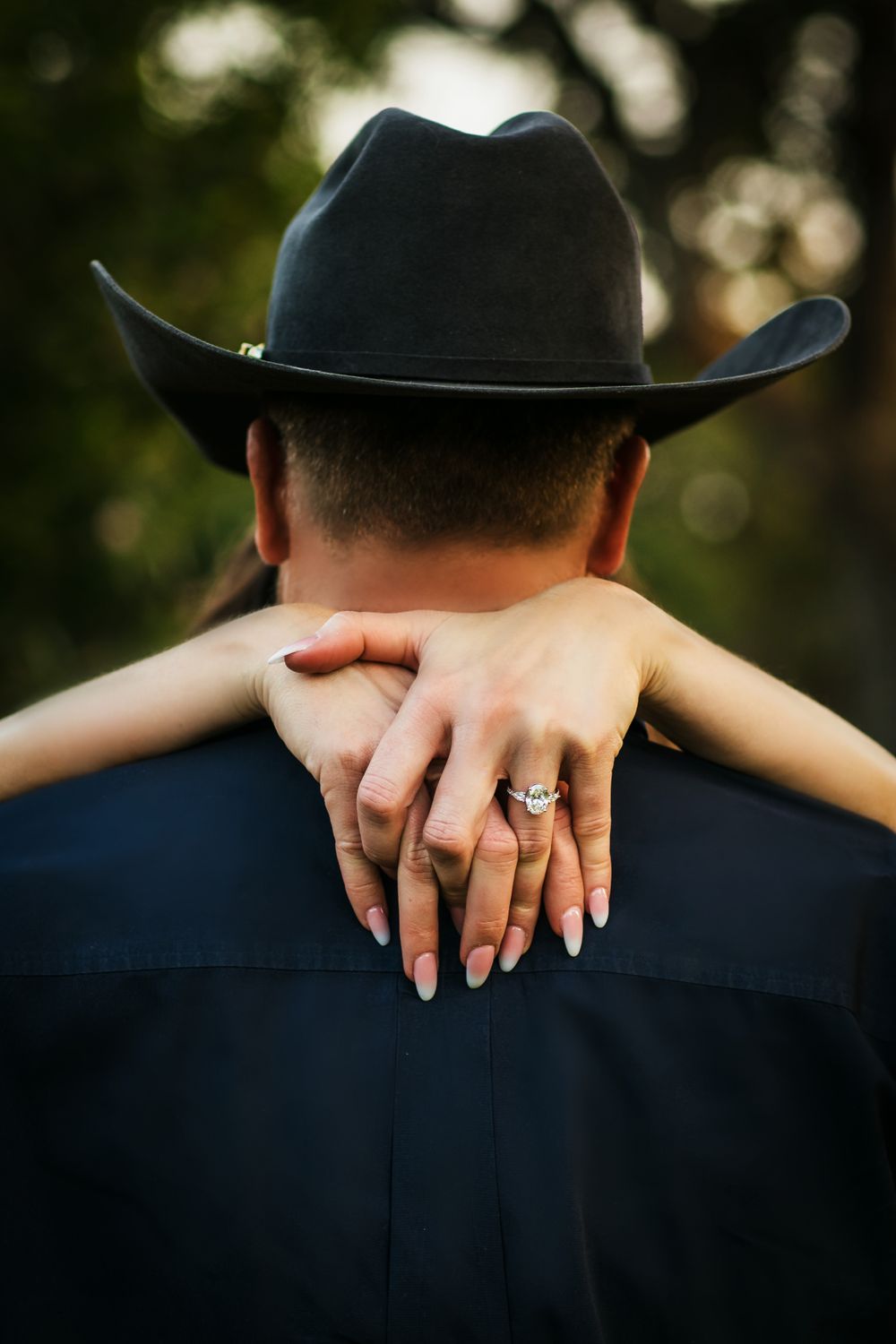 Close up of hands with engagement ring wrapped around person wearing black cowboy hat.