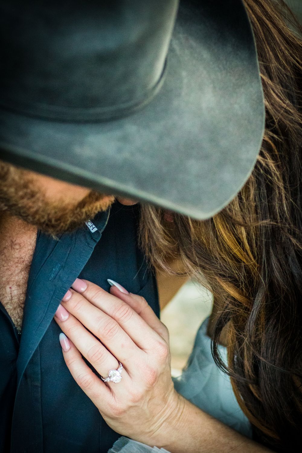 Close-up detail of a cowboy hat and engagement ring during a romantic moment.