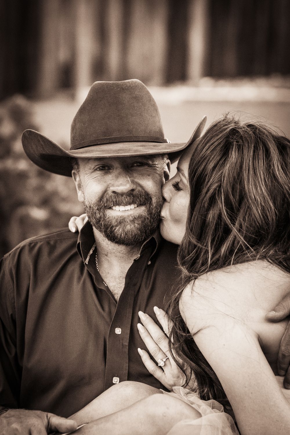 A romantic western-themed sepia photograph featuring a cowboy hat and tender moment.
