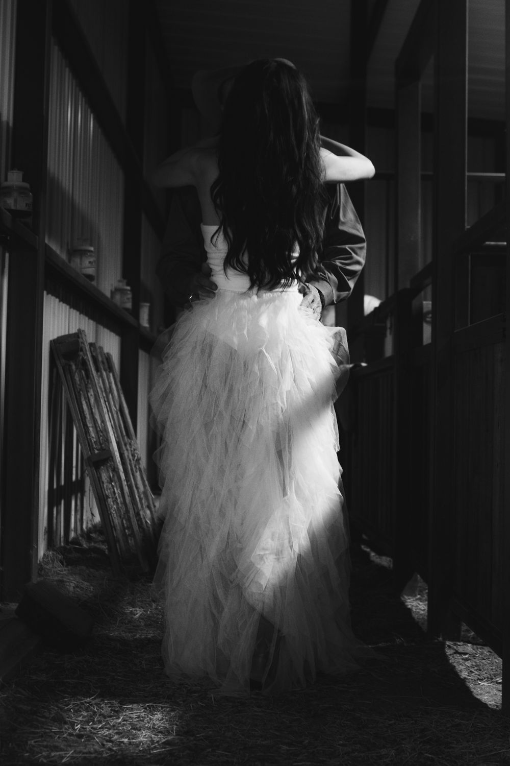 Silhouette of a bride in a flowing white wedding dress standing in a dark rustic hallway.