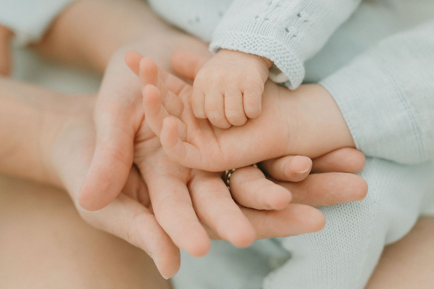 Close-up of adult and baby hands touching tenderly on soft white fabric.