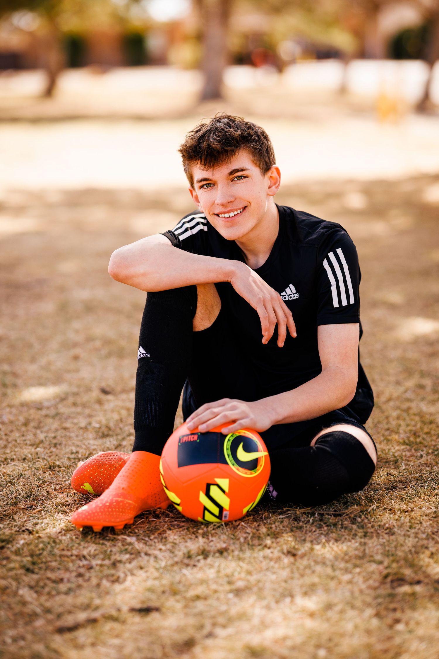 An athlete in Adidas clothing sits on grass with an orange soccer ball.