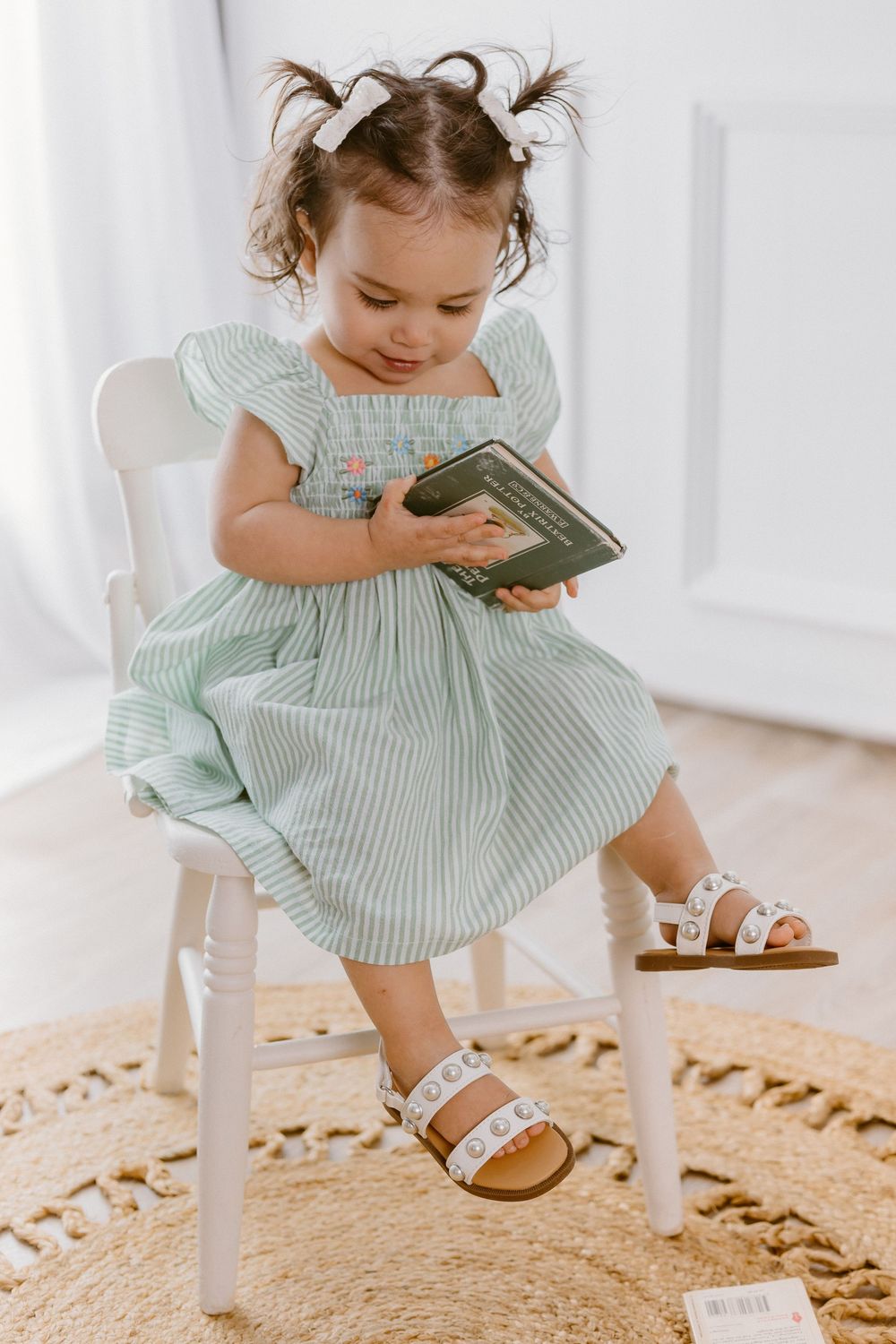 Sweet portrait of toddler in mint striped dress playing with toys on round jute rug.