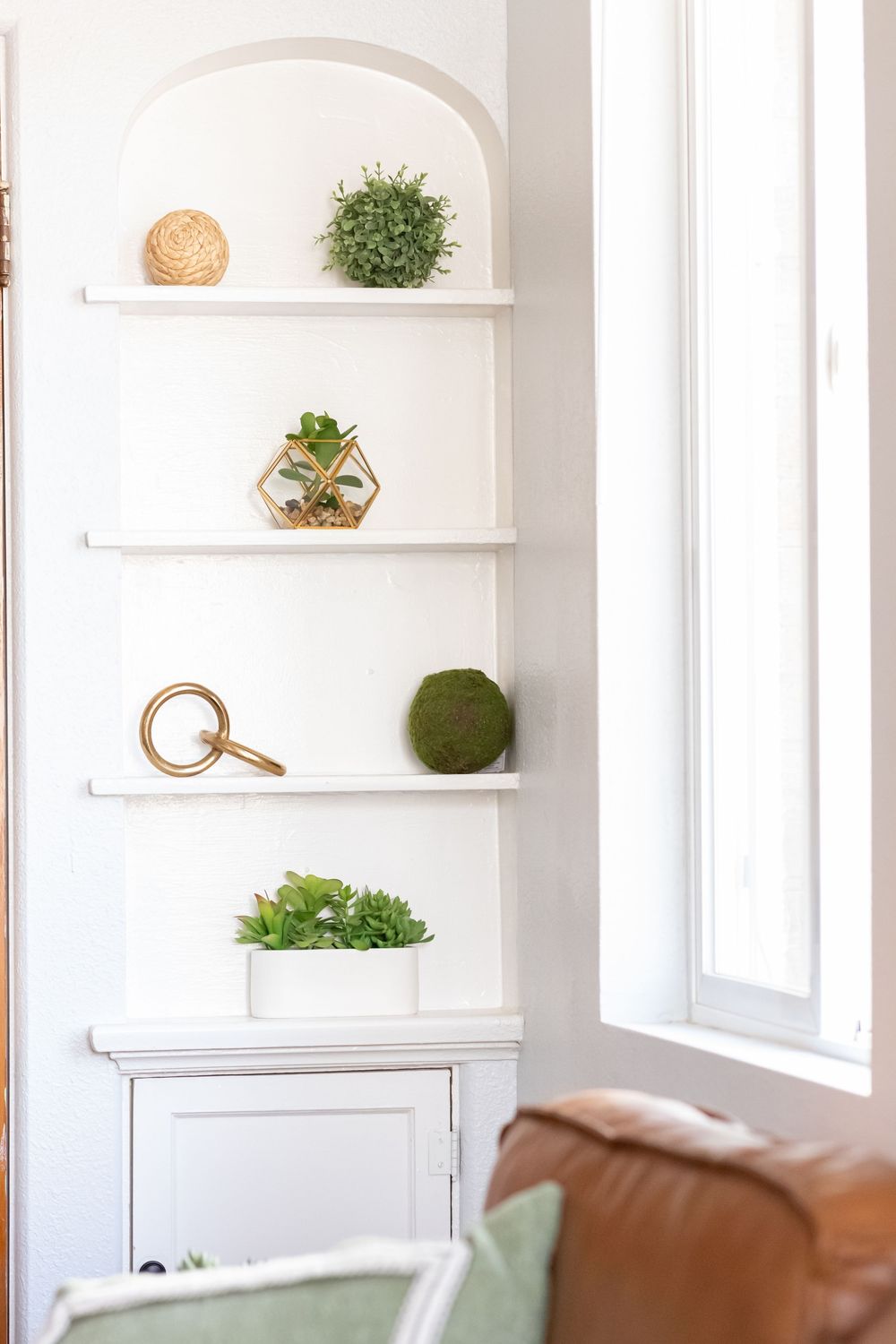 Modern white interior with built-in arched shelving displaying plants and decorative objects.