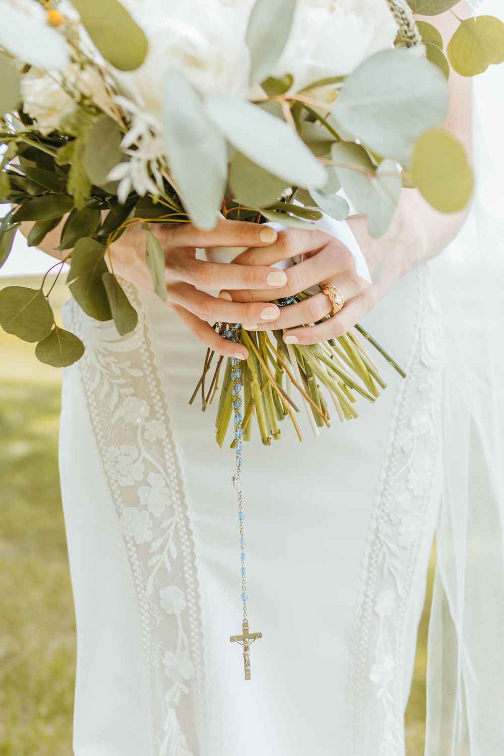 Close-up of bride holding white wedding bouquet with cross necklace detail.
