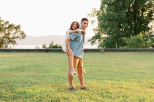Playful piggyback ride in a sunny meadow with mountains visible behind.