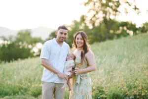 Family portrait with parents and baby outdoors in sunlit meadow.
