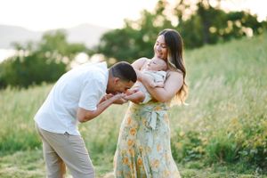 Tender family moment captured in sunlit meadow with floral dress and white shirt.