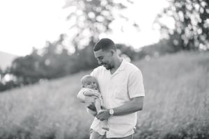 Black and white portrait of father holding infant in outdoor setting.