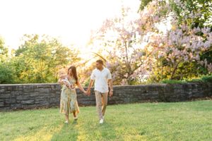 Couple strolling along stone wall with blooming trees in evening light.