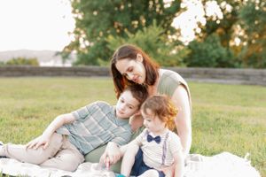 Three people sit close together on a blanket in a grassy field.