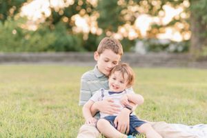 A couple plays with a small child during sunset near a stone wall.