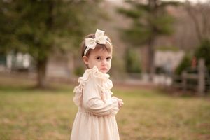 A series of seven sepia-toned photos showing a toddler in a vintage-style dress playing outdoors in a grassy field.