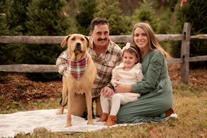 A happy family and their golden retriever dog enjoy a fall photoshoot outdoors by a rustic wooden fence.