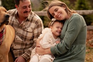 A joyful outdoor family portrait session features candid moments and laughter near a wooden fence in autumn.