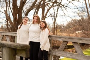 Two people in white sweaters share a laugh while sitting together on a wooden bench in an autumn outdoor setting.